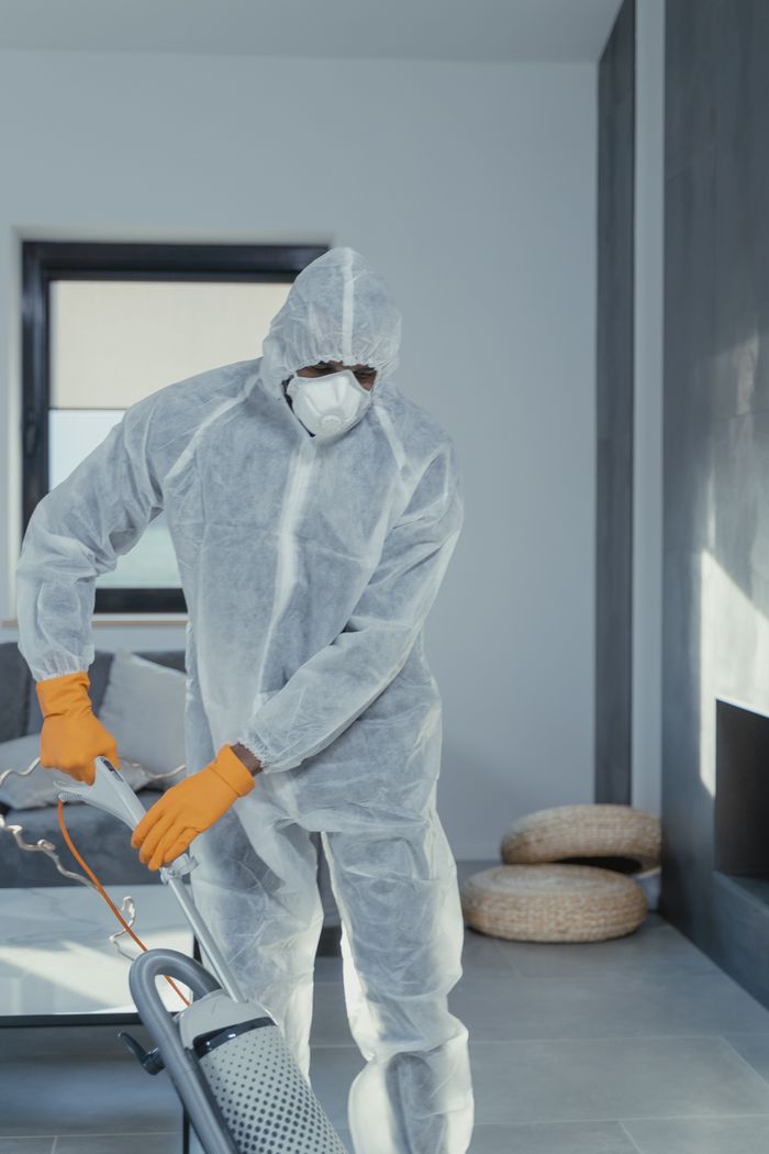 An individual wearing personal protective equipment is vacuuming inside, making sure the area is cleaned thoroughly.
